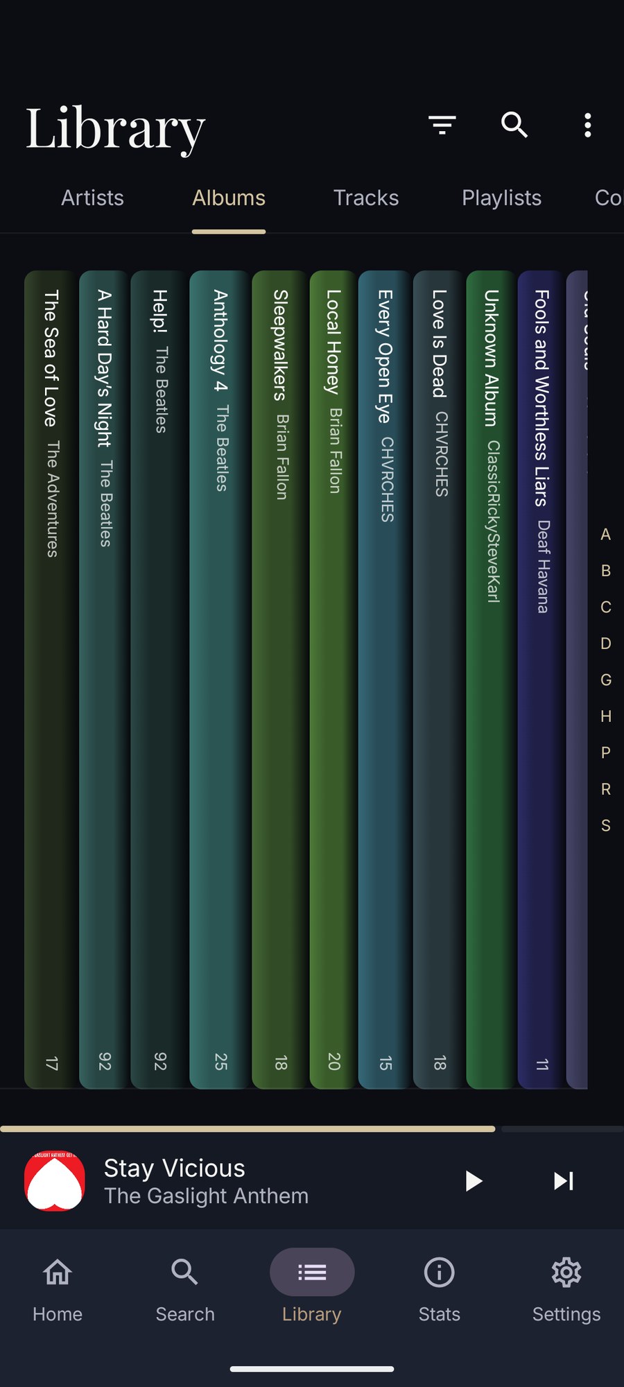 The Android album library as a shelf of coloured spines, each carrying the album title, artist and track count, with an A to Z index down the side.